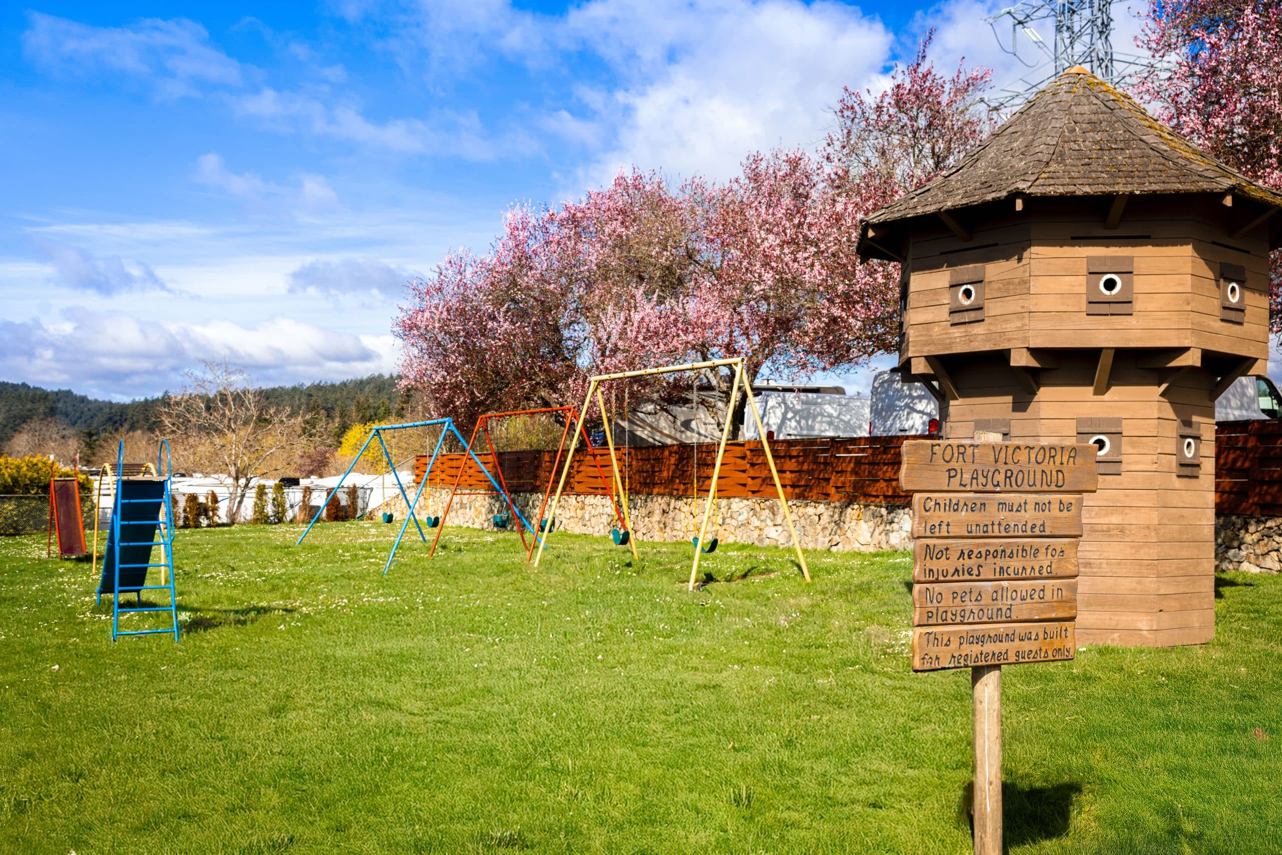 Playground beside the historic blockhouse at Fort Victoria RV Park with cherry blossoms.